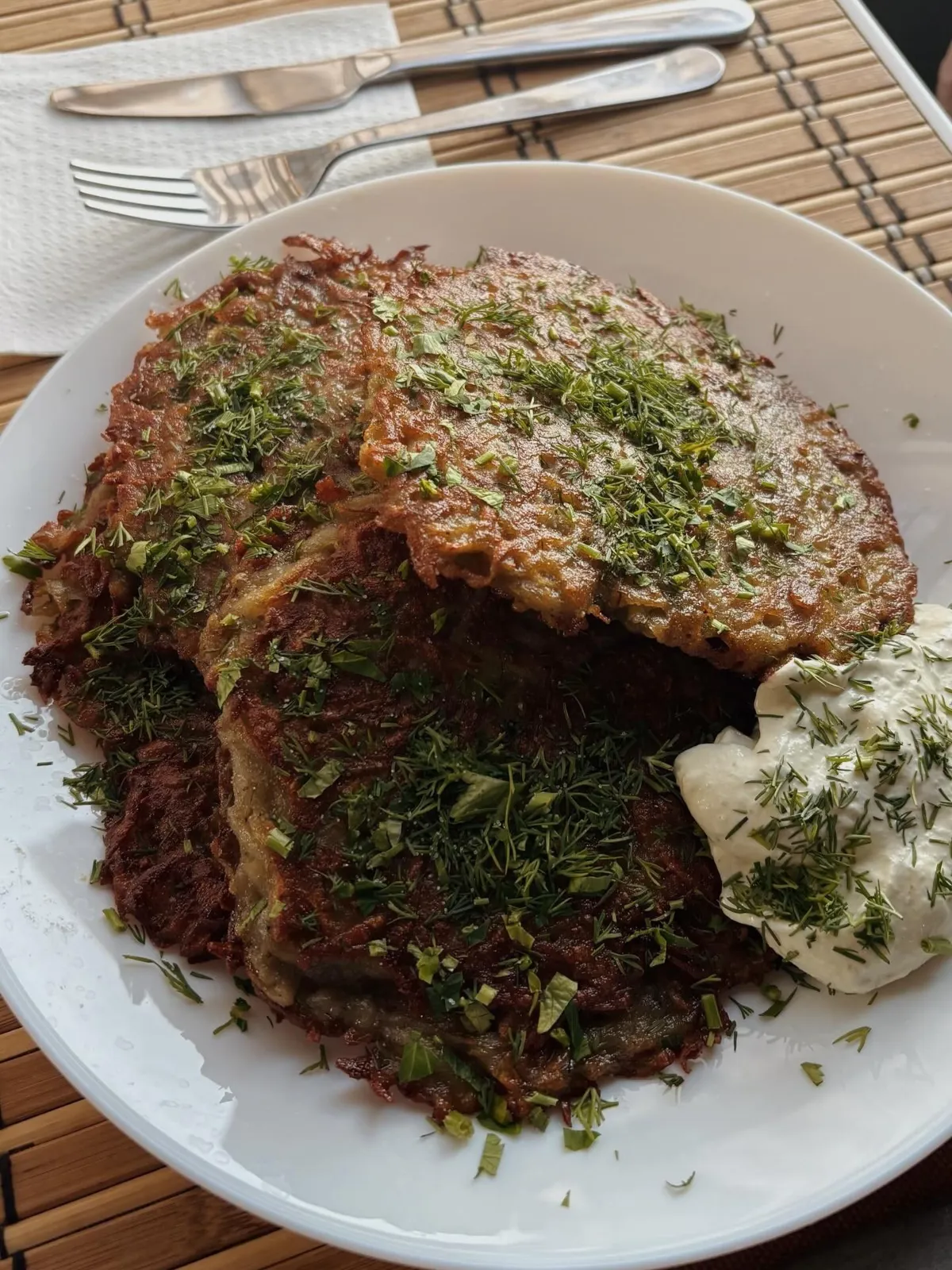 Kartupeļu pankūkas ar dillēm un baltu mērci uz šķīvja
